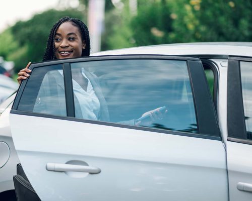 Portrait of successful african american business woman holding car door while getting inside. Attractive CEO black female executive wearing a suit and braids. Copy space. Successful woman in business.